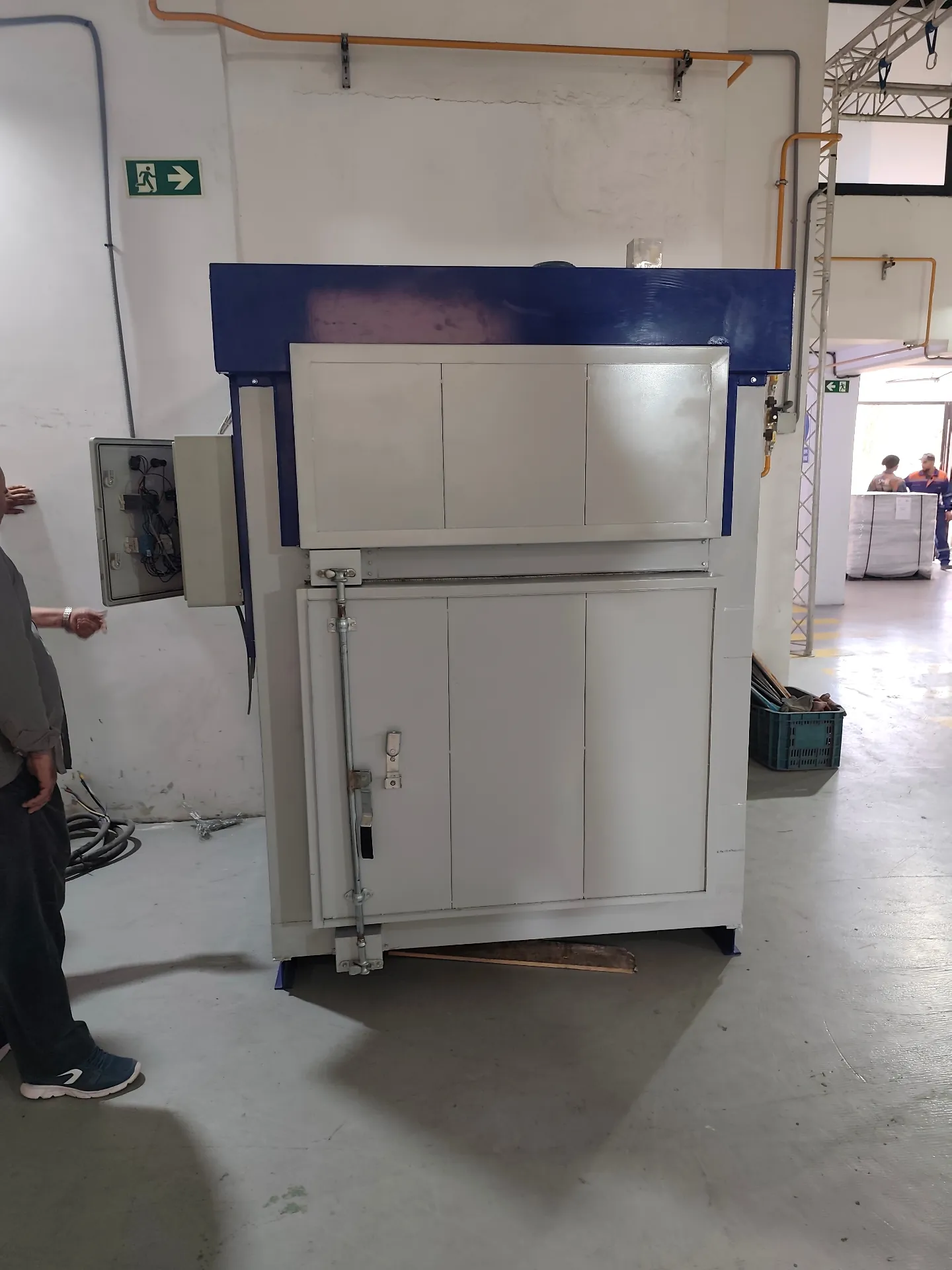 Four de thermolaquage industriel compact avec armoire électrique ouverte dans un atelier de fabrication.