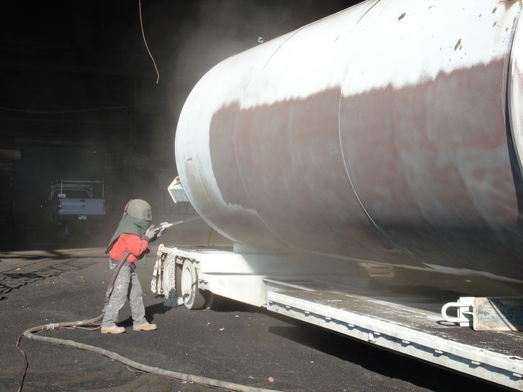 Opérateur équipé projetant de l'abrasif pour sabler une grande cuve métallique industrielle sur remorque.